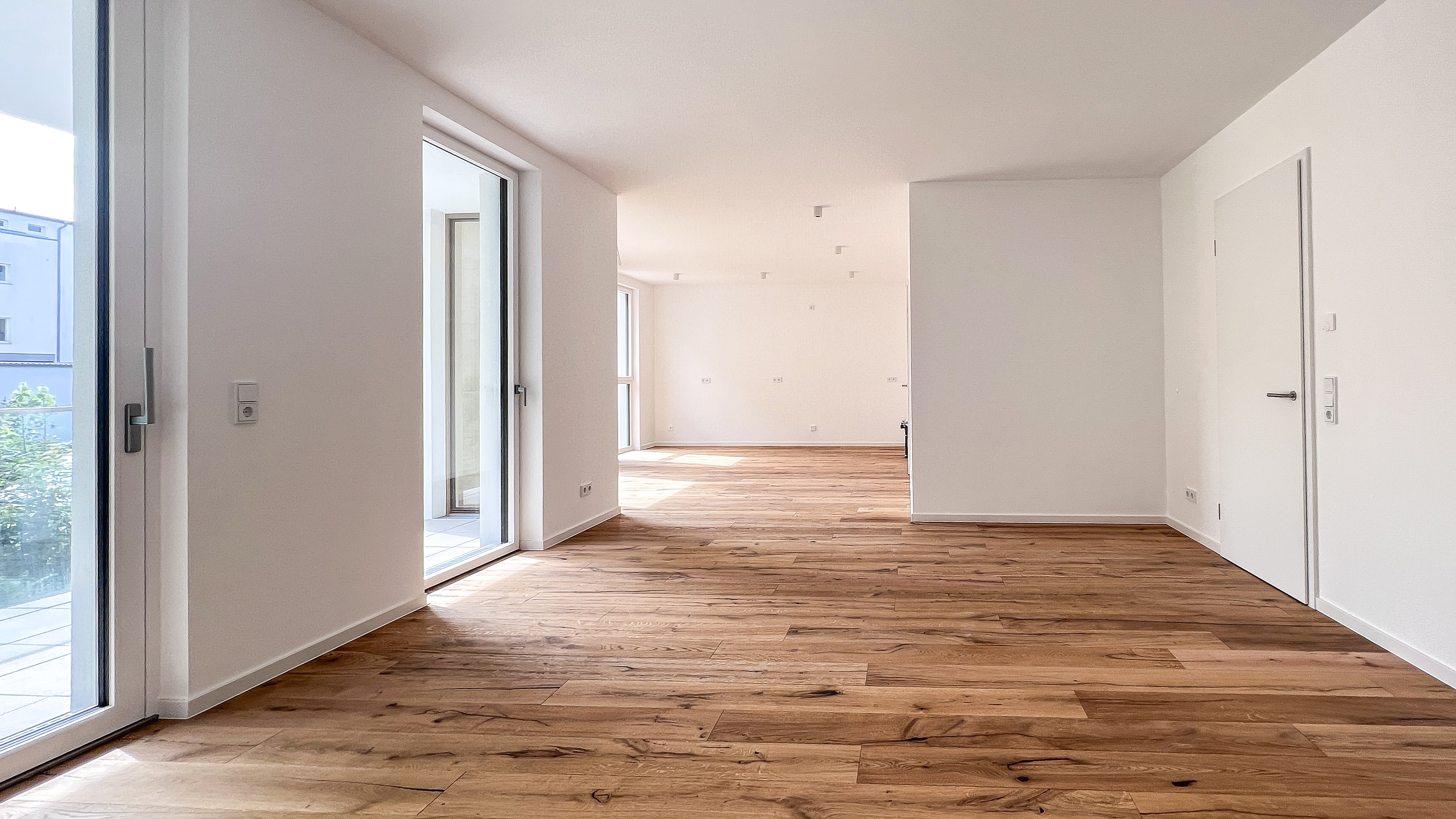 Helle, leere Neubauwohnung mit Eichenparkett, bodentiefen Fenstern und Zugang zur Terrasse in moderner Architektur.